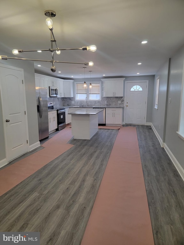 kitchen featuring a center island, dark wood-type flooring, stainless steel appliances, pendant lighting, and white cabinets