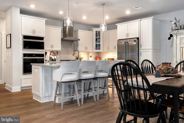 kitchen featuring white cabinetry, dark wood-type flooring, an island with sink, and hanging light fixtures