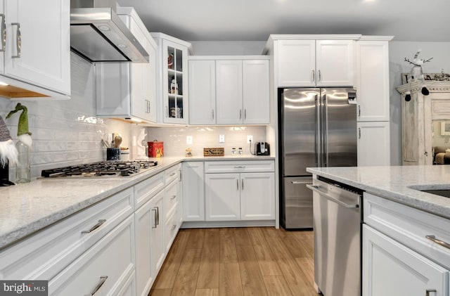 kitchen featuring appliances with stainless steel finishes, white cabinetry, and wall chimney range hood