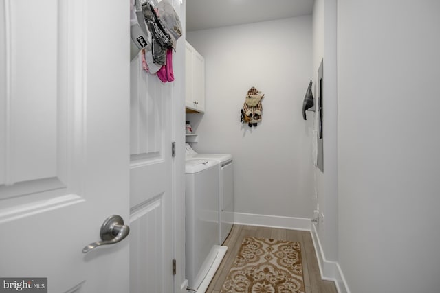 clothes washing area with cabinets, washing machine and dryer, and light hardwood / wood-style flooring