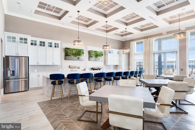 dining space with beamed ceiling, a high ceiling, ornamental molding, and coffered ceiling