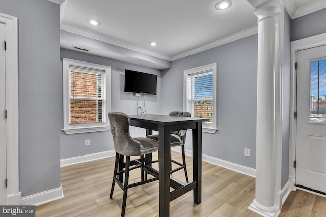 dining space featuring decorative columns, ornamental molding, and light wood-type flooring