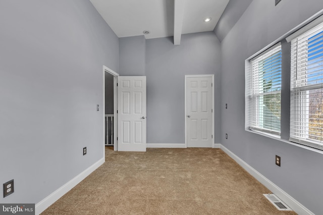 unfurnished bedroom featuring beamed ceiling, light carpet, and high vaulted ceiling