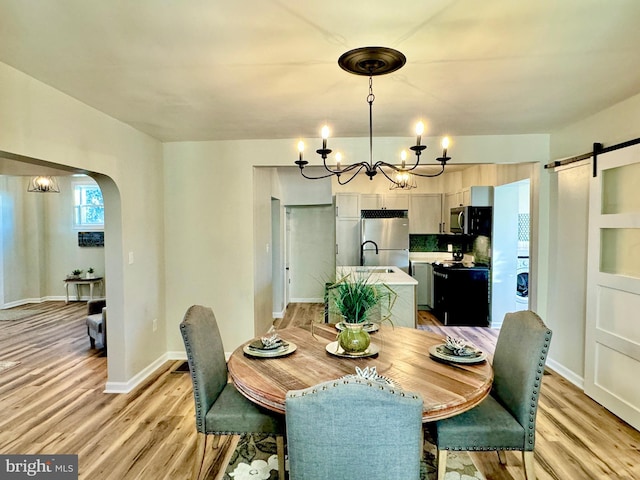 dining room with a barn door, light hardwood / wood-style floors, and an inviting chandelier