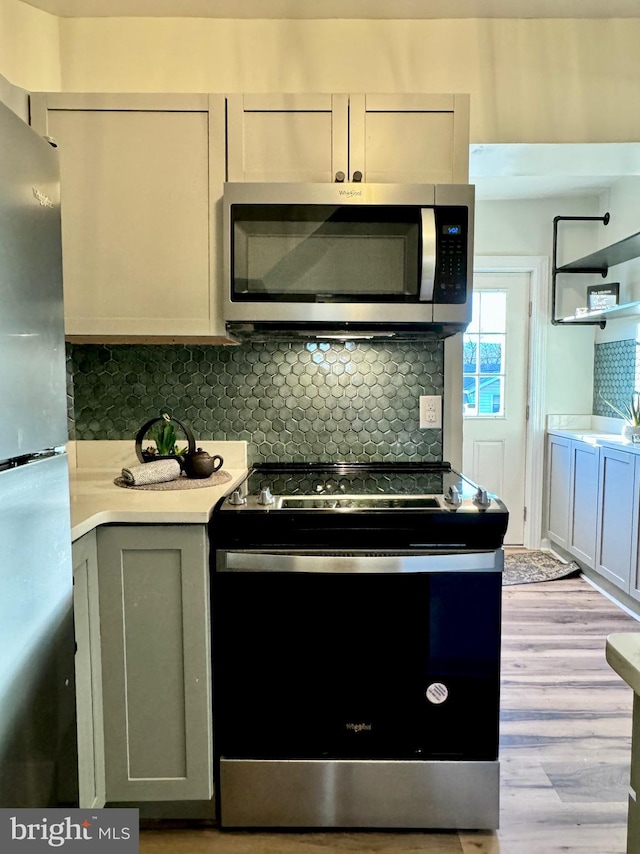 kitchen with gray cabinets, backsplash, appliances with stainless steel finishes, and light hardwood / wood-style flooring