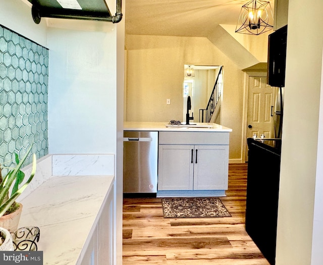 interior space featuring white cabinetry, sink, hanging light fixtures, stainless steel dishwasher, and light wood-type flooring