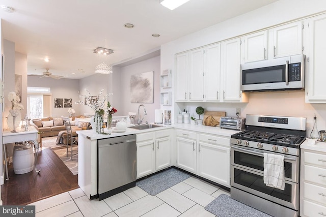 kitchen with white cabinetry, sink, stainless steel appliances, light hardwood / wood-style flooring, and kitchen peninsula