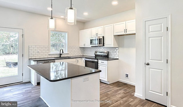 kitchen with sink, dark wood-type flooring, stainless steel appliances, decorative light fixtures, and white cabinets