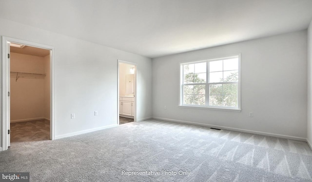 unfurnished bedroom featuring carpet flooring, ensuite bathroom, a spacious closet, and a closet