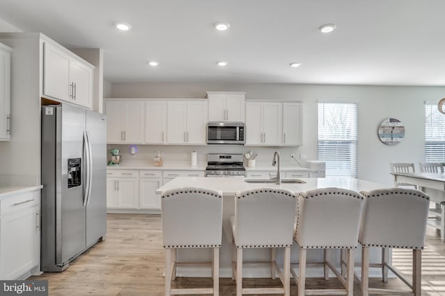 kitchen with sink, light hardwood / wood-style flooring, appliances with stainless steel finishes, a kitchen bar, and white cabinetry