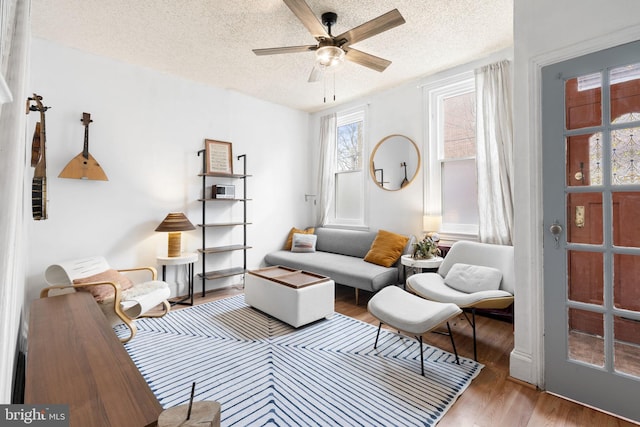 living room featuring wood-type flooring, ceiling fan, and a textured ceiling