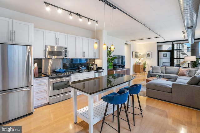 kitchen featuring light wood finished floors, dark countertops, appliances with stainless steel finishes, open floor plan, and a sink