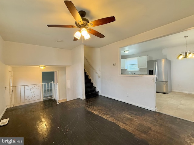 unfurnished living room featuring ceiling fan with notable chandelier and wood-type flooring