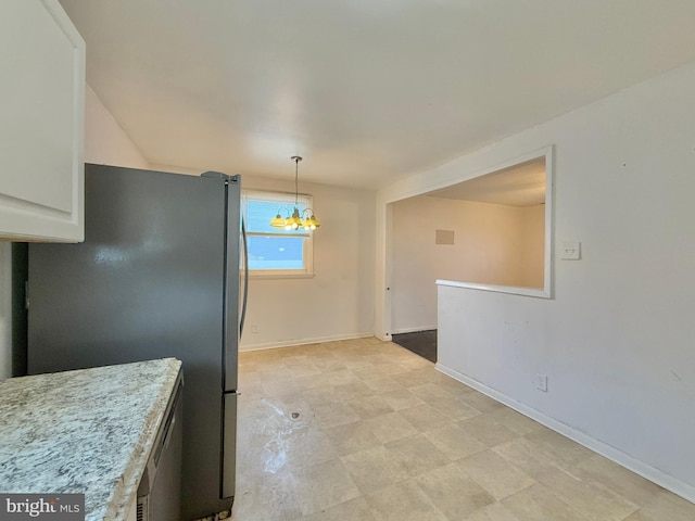 kitchen featuring white cabinets, light stone countertops, pendant lighting, a notable chandelier, and stainless steel fridge