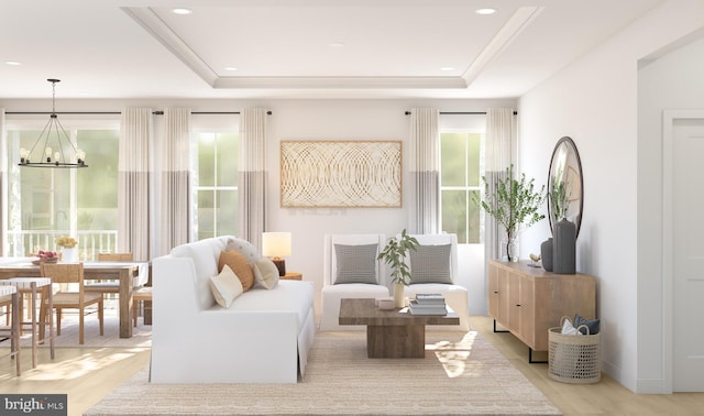 living room with a raised ceiling, light hardwood / wood-style floors, and a notable chandelier