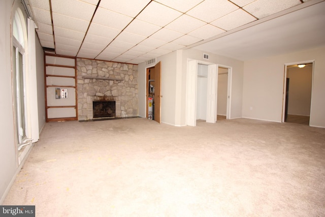 unfurnished living room with a stone fireplace, light carpet, and a paneled ceiling