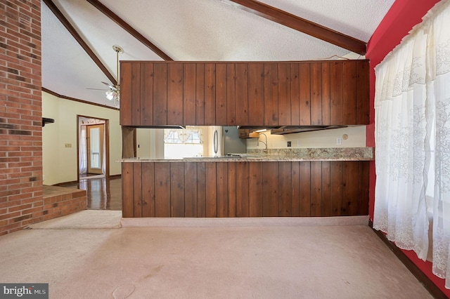 kitchen with wooden walls, carpet flooring, vaulted ceiling with beams, ceiling fan, and kitchen peninsula