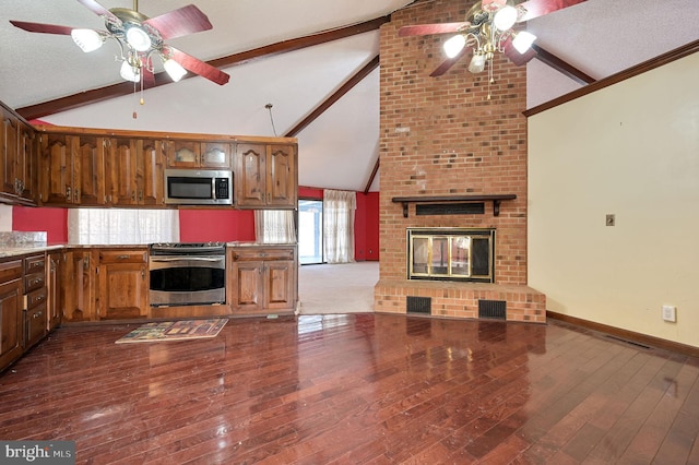 kitchen featuring stainless steel appliances, a brick fireplace, a textured ceiling, and vaulted ceiling with beams