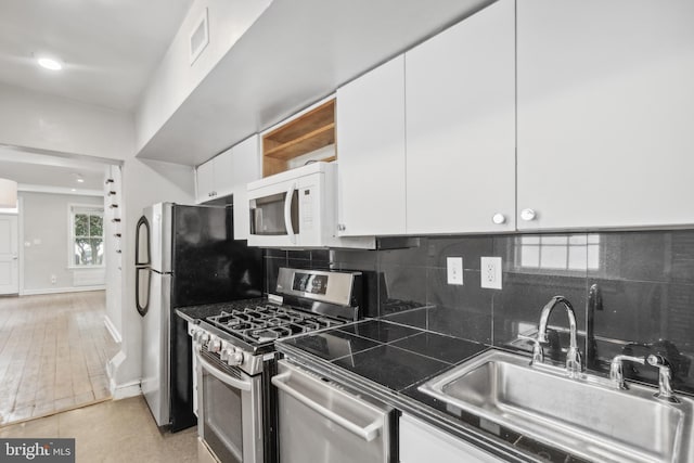 kitchen with white cabinets, sink, decorative backsplash, light tile patterned floors, and appliances with stainless steel finishes