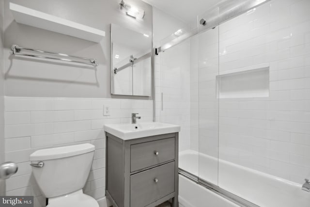 full bathroom with shower / bath combination with glass door, vanity, toilet, and tile walls