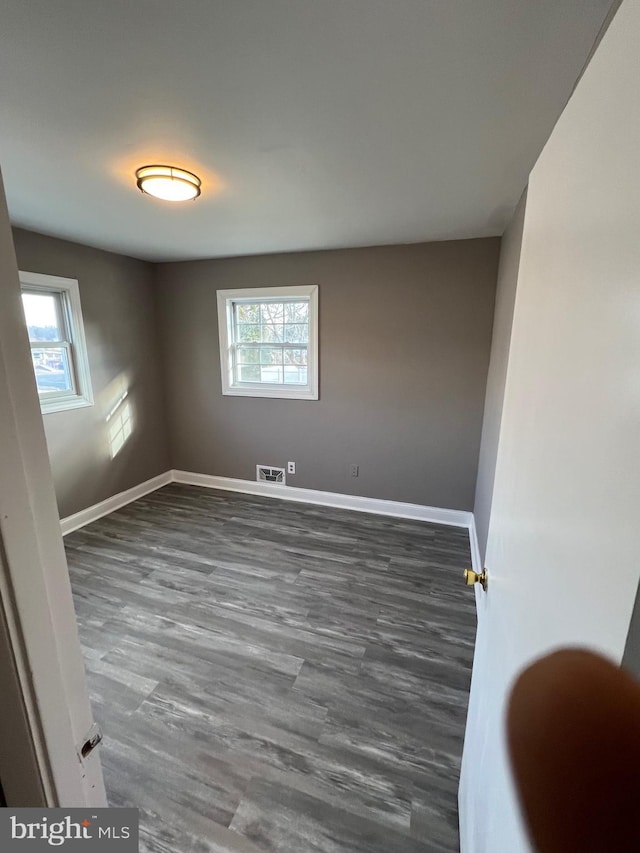 empty room with dark hardwood / wood-style flooring and a wealth of natural light