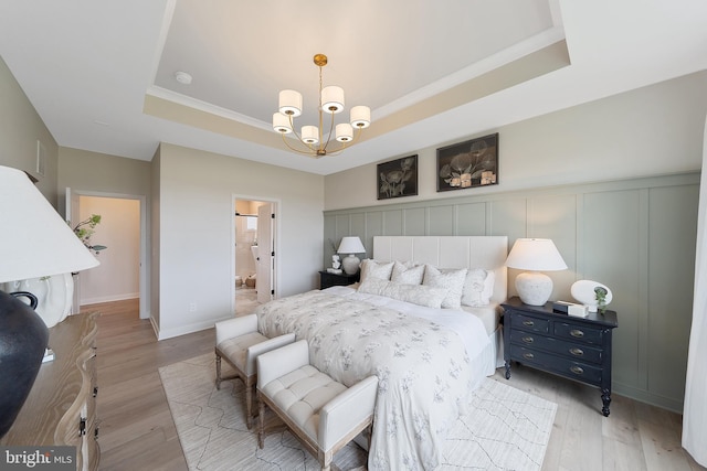 bedroom with a tray ceiling, ensuite bath, and light hardwood / wood-style flooring