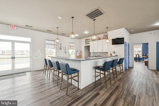 kitchen with dark wood-type flooring, a kitchen breakfast bar, hanging light fixtures, white cabinetry, and kitchen peninsula