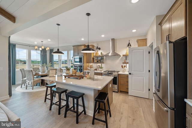 kitchen featuring pendant lighting, a spacious island, wall chimney range hood, appliances with stainless steel finishes, and light hardwood / wood-style floors