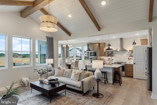 living room featuring vaulted ceiling with beams, light hardwood / wood-style floors, an inviting chandelier, and a healthy amount of sunlight