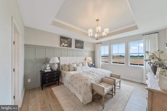 bedroom featuring light wood-type flooring, a tray ceiling, and an inviting chandelier