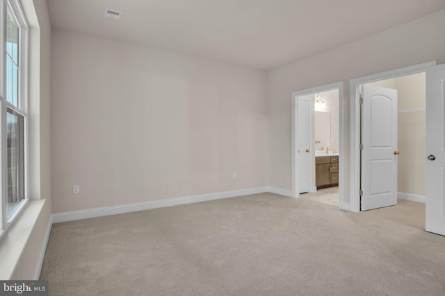 unfurnished bedroom featuring a spacious closet, light carpet, connected bathroom, and a closet