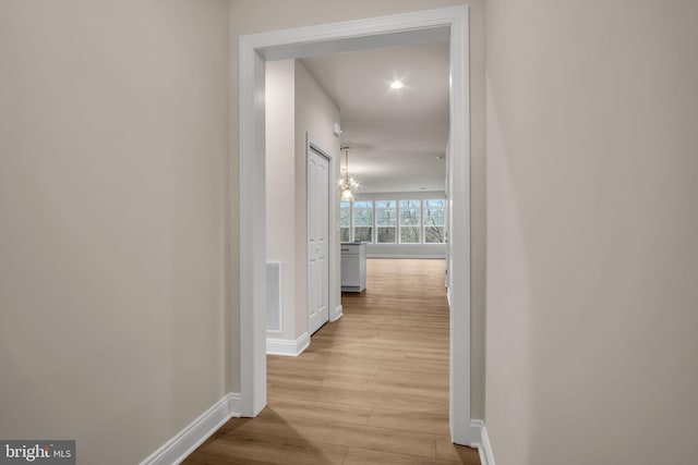 hallway featuring light wood-type flooring and an inviting chandelier