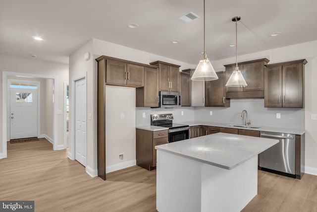 kitchen featuring pendant lighting, a center island, sink, light wood-type flooring, and appliances with stainless steel finishes