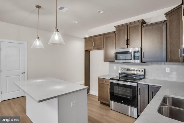 kitchen with light stone counters, light wood-type flooring, stainless steel appliances, and hanging light fixtures