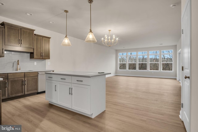 kitchen with pendant lighting, sink, light hardwood / wood-style flooring, stainless steel dishwasher, and decorative backsplash