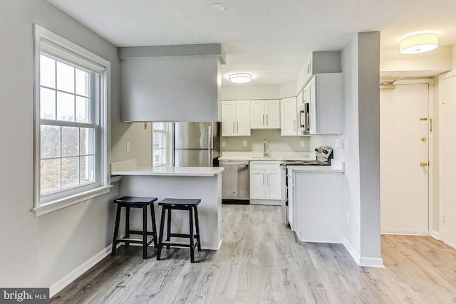 kitchen with white cabinetry, stainless steel appliances, kitchen peninsula, a breakfast bar, and light wood-type flooring