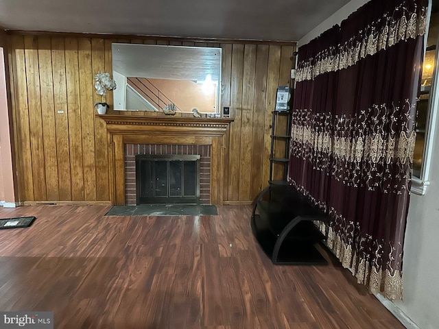 living room with wood walls, dark wood-type flooring, and a brick fireplace