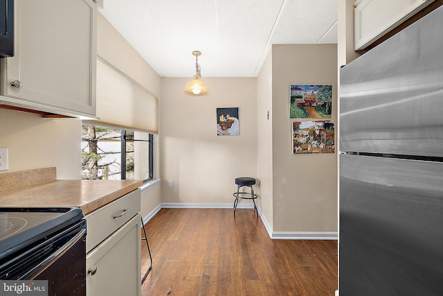 kitchen with stainless steel fridge, black range with electric cooktop, decorative light fixtures, and hardwood / wood-style flooring