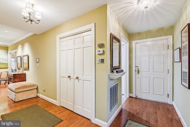 foyer featuring wood-type flooring, crown molding, and an inviting chandelier