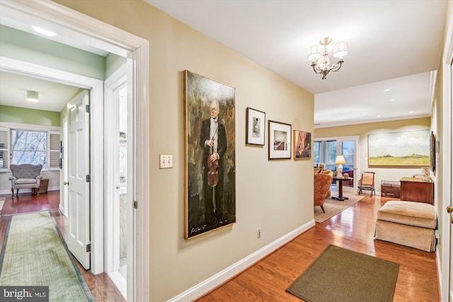 corridor with hardwood / wood-style floors and an inviting chandelier