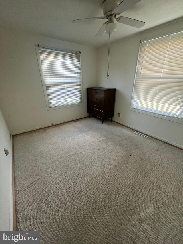 carpeted empty room with ceiling fan and plenty of natural light