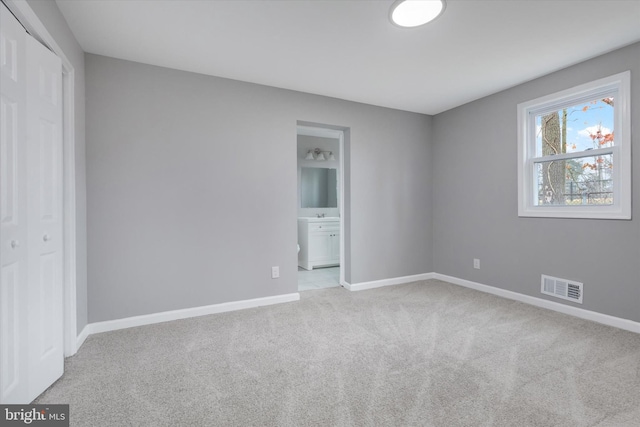 unfurnished bedroom featuring ensuite bath, light carpet, and a closet