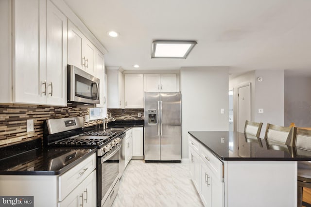 kitchen with decorative backsplash, appliances with stainless steel finishes, a kitchen breakfast bar, sink, and white cabinetry