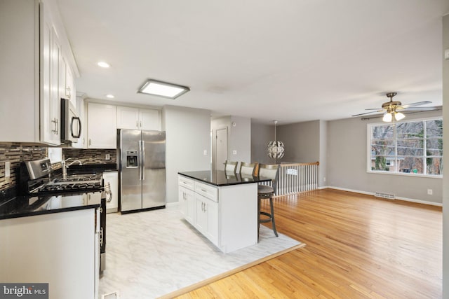 kitchen with a center island, stainless steel appliances, light hardwood / wood-style flooring, a breakfast bar, and white cabinets