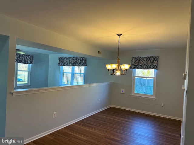 empty room with dark wood-type flooring and an inviting chandelier