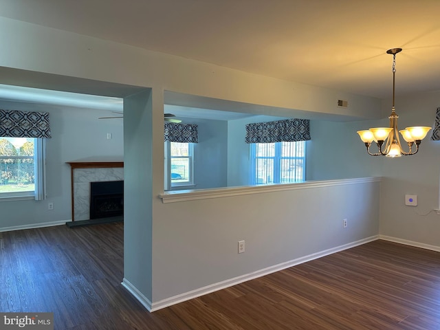 unfurnished room featuring a premium fireplace, dark wood-type flooring, and ceiling fan with notable chandelier