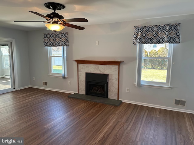 unfurnished living room featuring a tile fireplace, dark hardwood / wood-style flooring, plenty of natural light, and ceiling fan