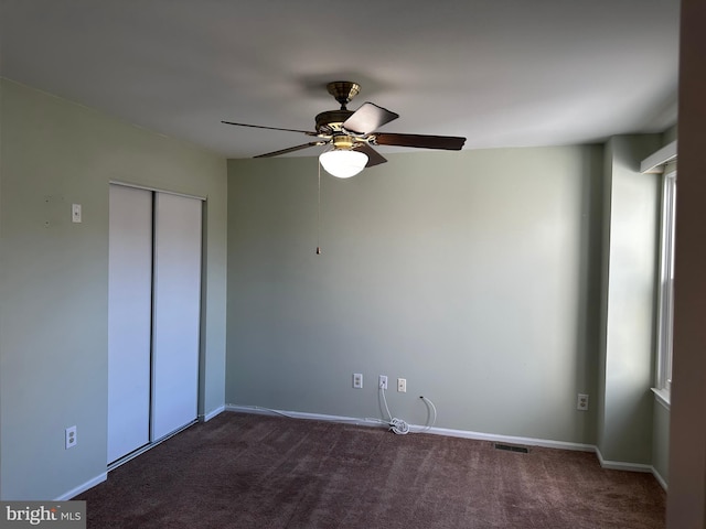 unfurnished bedroom with dark colored carpet, ceiling fan, and a closet