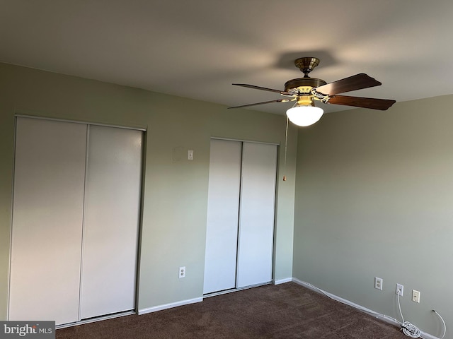 unfurnished bedroom featuring ceiling fan, two closets, and dark colored carpet