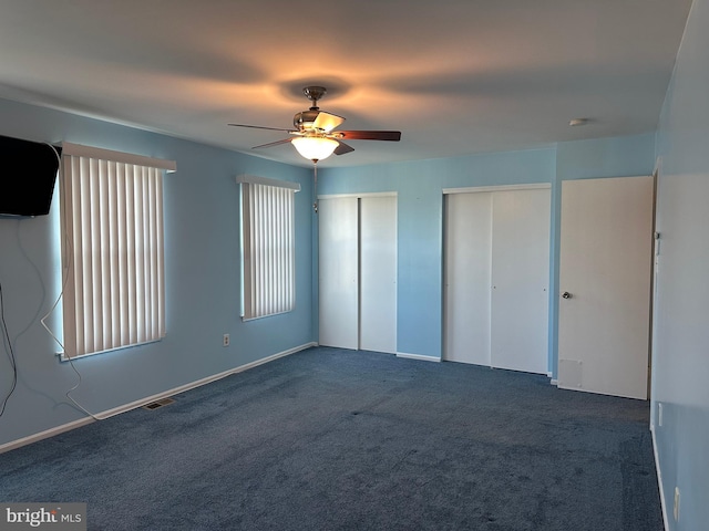 unfurnished bedroom with multiple closets, ceiling fan, and dark colored carpet